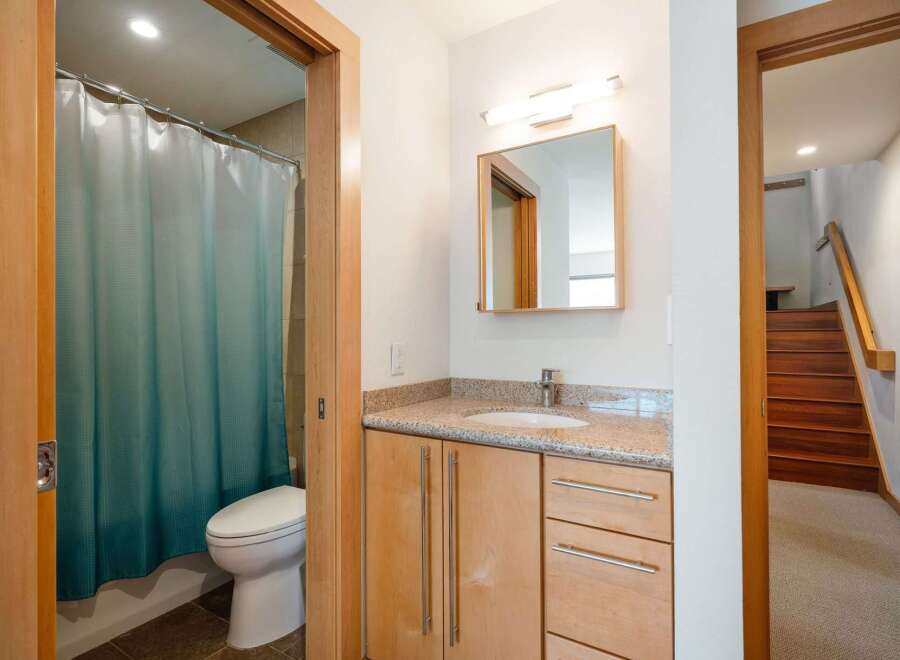 This modern bathroom features a sleek vanity with a granite countertop and ample storage, complemented by a stylish mirror and lighting.