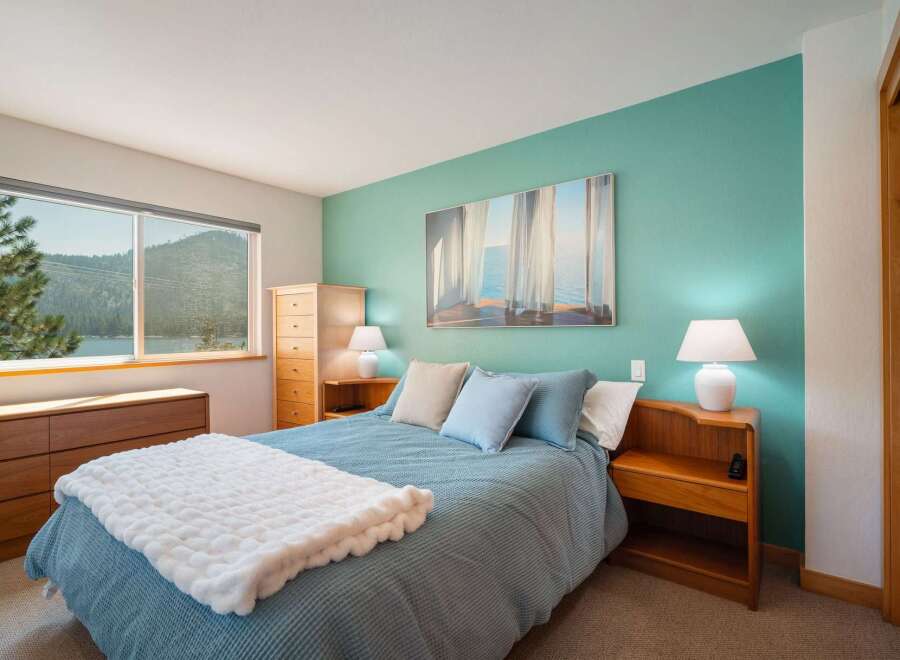 Experience serene lake views from this charming bedroom, featuring a comfortable queen-size bed adorned with a plush white throw.