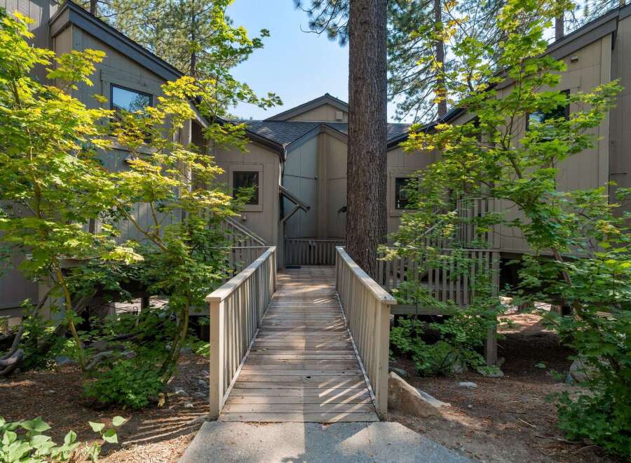 Discover this charming property featuring a welcoming wooden walkway leading to the entrance, surrounded by lush greenery and mature trees.