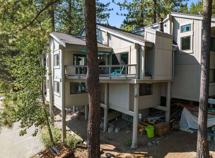 Nestled among tall pine trees, this multi-level home offers a unique architectural style with a light-colored exterior and a spacious deck perfect for enjoying the natural surroundings.