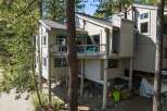 Nestled among tall pine trees, this multi-level home offers a unique architectural style with a light-colored exterior and a spacious deck perfect for enjoying the natural surroundings.