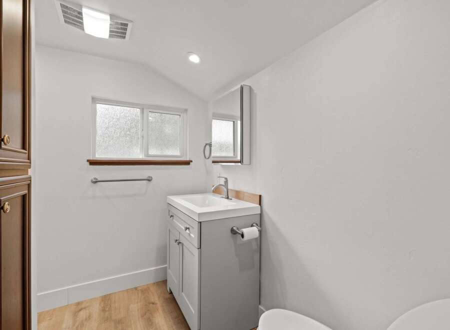 This bright and airy bathroom features a modern gray vanity with a white countertop and a sleek chrome faucet.
