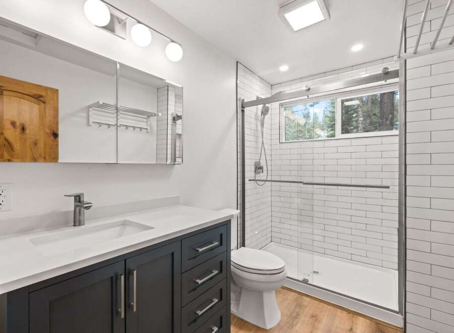 This modern bathroom features a sleek vanity with a white countertop and dark cabinets, complemented by a spacious walk-in shower with white subway tiles.