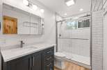This modern bathroom features a sleek vanity with a white countertop and dark cabinets, complemented by a spacious walk-in shower with white subway tiles.