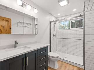 This modern bathroom features a sleek vanity with a white countertop and dark cabinets, complemented by a spacious walk-in shower with white subway tiles.