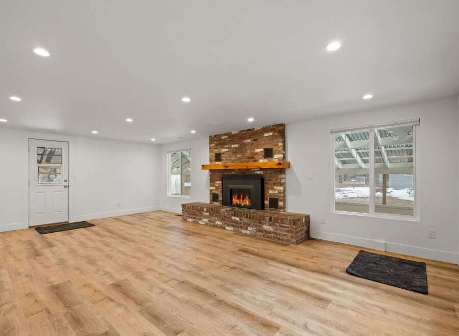 Experience cozy living in this spacious room featuring a striking brick fireplace with a rustic wooden mantel, perfect for gathering on chilly evenings.