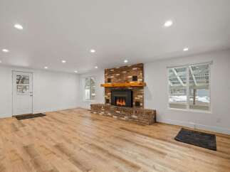 Experience cozy living in this spacious room featuring a striking brick fireplace with a rustic wooden mantel, perfect for gathering on chilly evenings.
