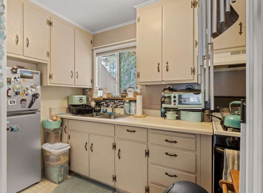Charming kitchen featuring cream-colored cabinetry and a double sink beneath a window overlooking greenery.
