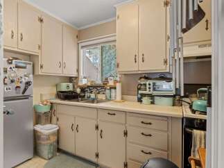 Charming kitchen featuring cream-colored cabinetry and a double sink beneath a window overlooking greenery.