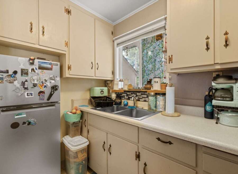 This charming kitchen features a double sink beneath a window with decorative curtains, offering a bright and airy feel.