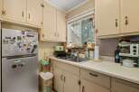 This charming kitchen features a double sink beneath a window with decorative curtains, offering a bright and airy feel.