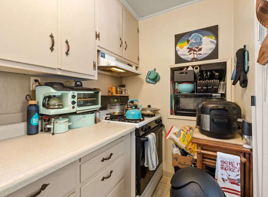 Discover this charming kitchen, perfect for home chefs! It features a compact gas stove with a blue kettle and pots, a retro-style coffee maker and toaster oven, and ample counter space for meal prep.