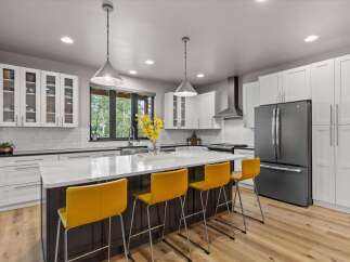Experience modern luxury in this stunning kitchen, featuring sleek white cabinetry, a spacious quartz island with seating, and a professional-grade stainless steel range hood.