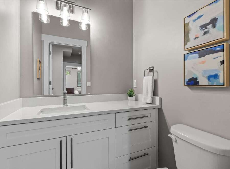 This modern bathroom features a sleek white vanity with ample storage and a quartz countertop, complemented by a large vanity mirror with contemporary lighting.