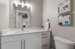 This modern bathroom features a sleek white vanity with ample storage and a quartz countertop, complemented by a large vanity mirror with contemporary lighting.