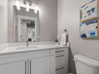 This modern bathroom features a sleek white vanity with ample storage and a quartz countertop, complemented by a large vanity mirror with contemporary lighting.