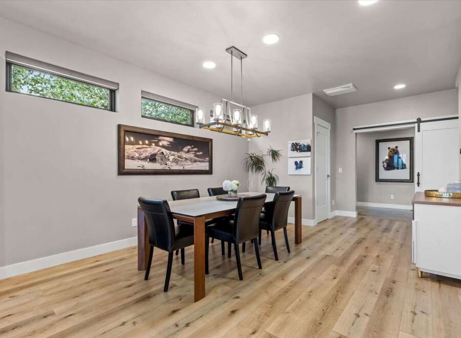 This modern dining room features a sleek rectangular dining table with black leather chairs, illuminated by a contemporary chandelier.