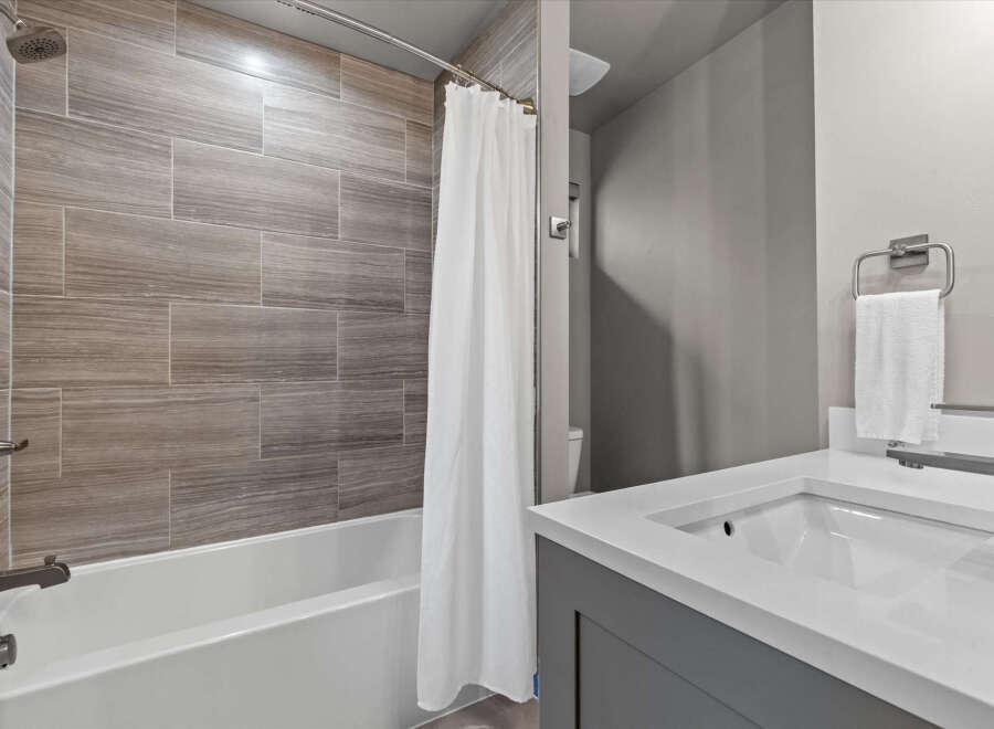 Experience modern comfort in this beautifully appointed bathroom, featuring elegant wood-look tile shower walls and a sleek white bathtub.