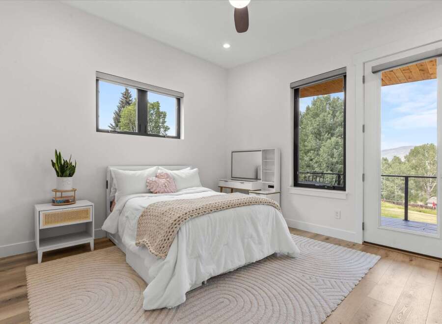 Experience modern comfort in this bright bedroom featuring a plush white bed adorned with a cozy knit throw and decorative pillows.