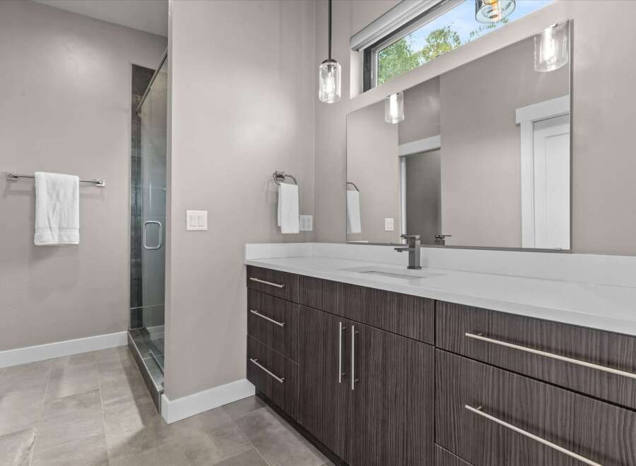 Experience modern luxury in this stunning bathroom featuring a sleek vanity with ample storage and a spacious glass-enclosed shower.