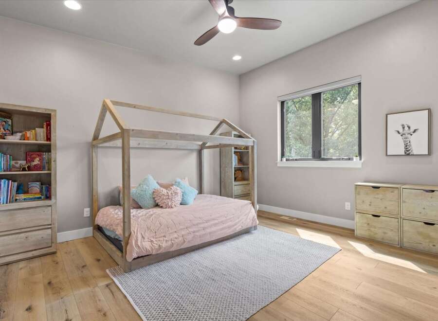 This charming children's bedroom features a whimsical house-shaped bed with a pink comforter and plush pillows, creating a cozy and inviting sleep space.