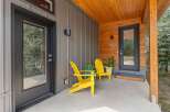 Welcome guests to this modern home with a charming covered porch featuring two bright yellow Adirondack chairs and lush potted plants.