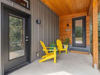 Welcome guests to this modern home with a charming covered porch featuring two bright yellow Adirondack chairs and lush potted plants.