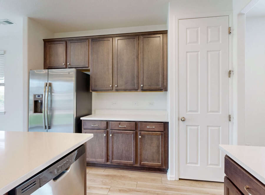 This modern kitchen features sleek, dark wood cabinetry complemented by a bright white countertop and stainless steel appliances, including a refrigerator and dishwasher.
