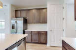 This modern kitchen features sleek, dark wood cabinetry complemented by a bright white countertop and stainless steel appliances, including a refrigerator and dishwasher.