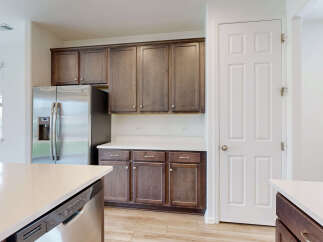 This modern kitchen features sleek, dark wood cabinetry complemented by a bright white countertop and stainless steel appliances, including a refrigerator and dishwasher.