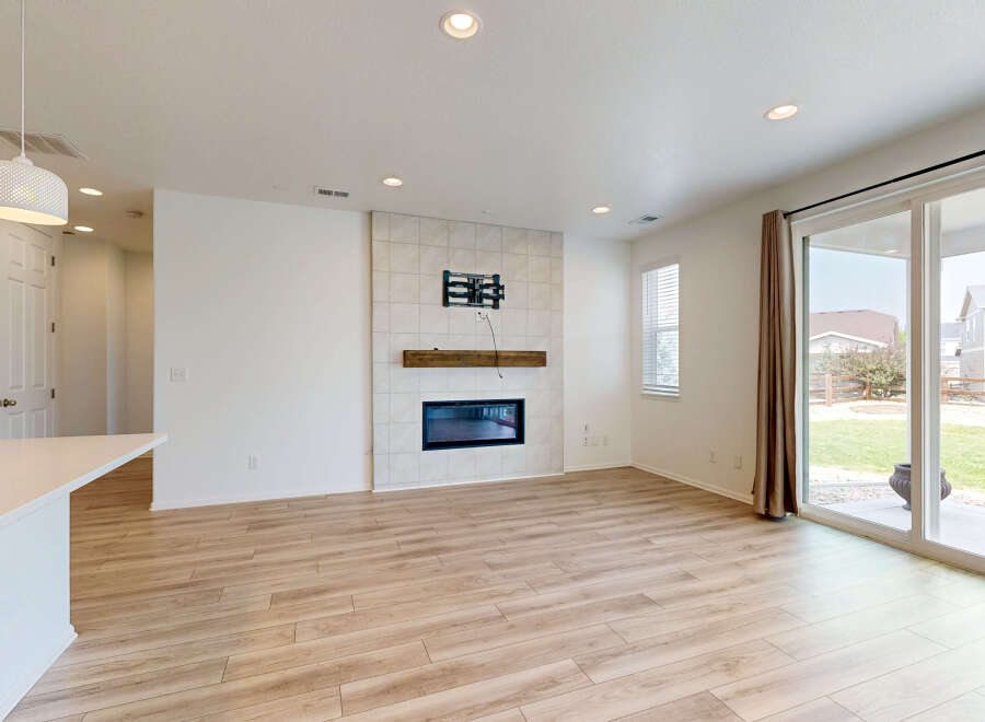 Experience modern living in this spacious great room featuring a sleek fireplace with a tiled surround and a rustic wooden mantel.