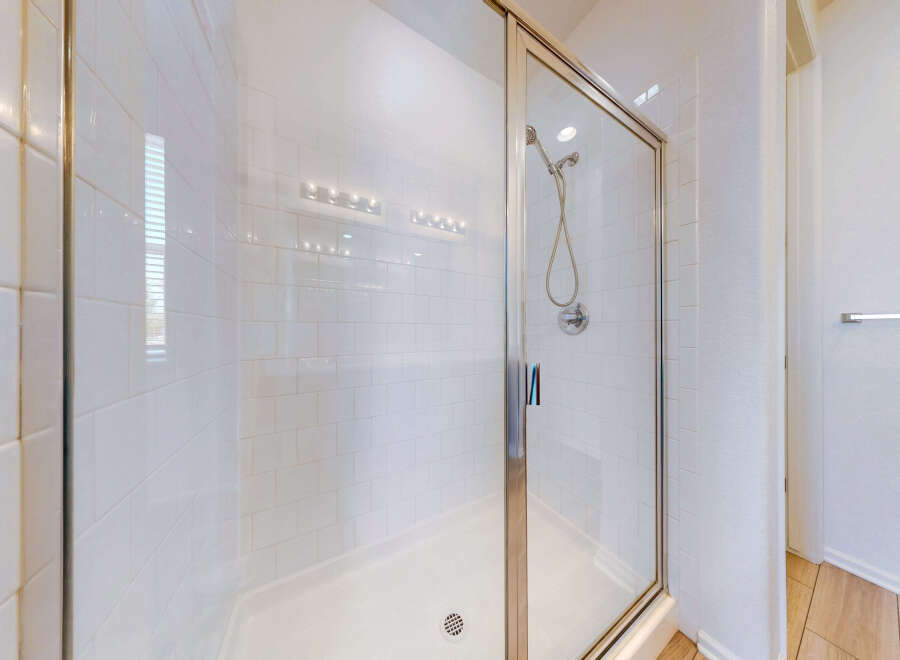 Step into this pristine white tiled shower, featuring a sleek glass enclosure and a modern chrome showerhead.