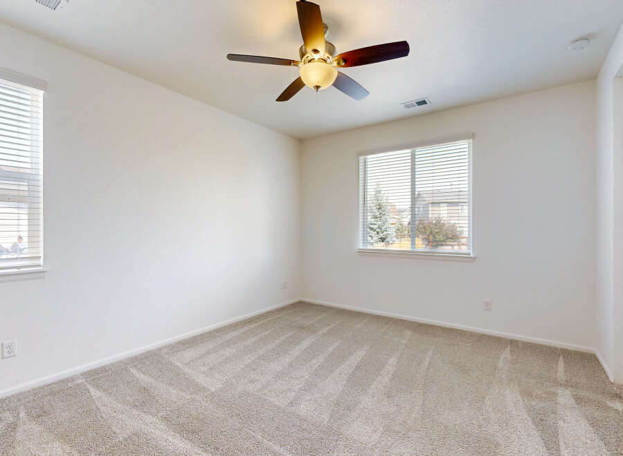 This spacious bedroom features plush carpeting and a ceiling fan for comfort.