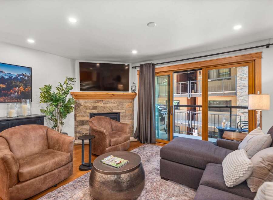 Experience modern mountain living in this beautifully appointed living room, featuring a cozy stone fireplace and a large flat-screen TV.