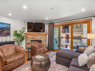 Experience modern mountain living in this beautifully appointed living room, featuring a cozy stone fireplace and a large flat-screen TV.