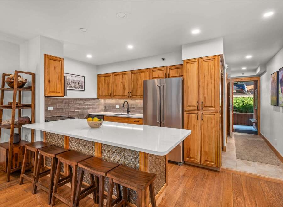 This stunning kitchen features warm, natural wood cabinetry that complements the sleek white countertops and modern stainless steel appliances.