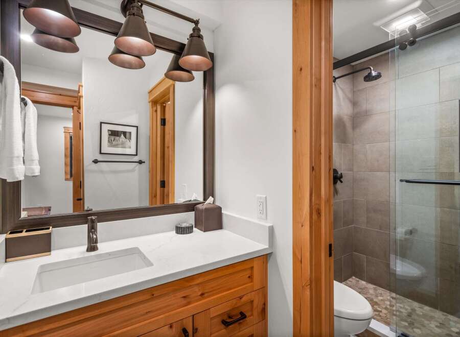 This modern bathroom features a sleek vanity with a white quartz countertop and a vessel sink, complemented by warm wood cabinetry.