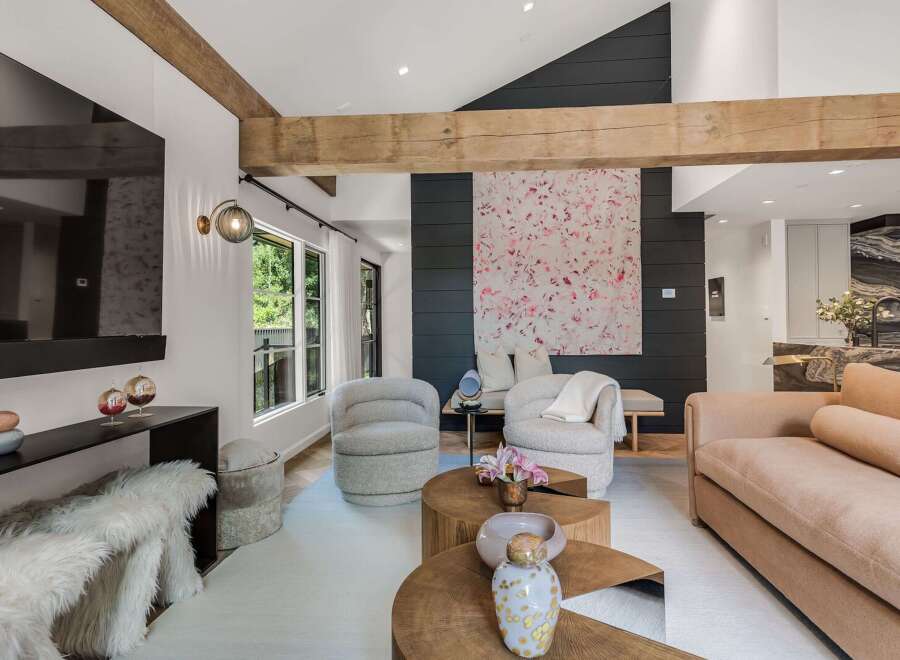 Experience modern luxury in this stunning living room, featuring a dramatic vaulted ceiling with exposed wooden beams and a striking abstract art piece.