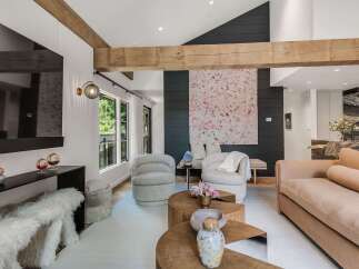 Experience modern luxury in this stunning living room, featuring a dramatic vaulted ceiling with exposed wooden beams and a striking abstract art piece.