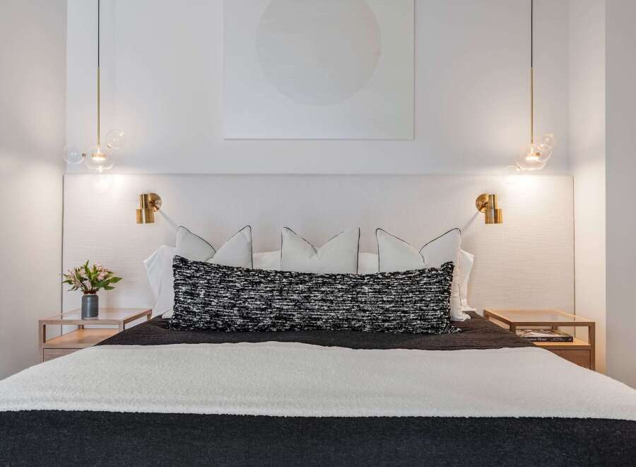 Experience modern luxury in this beautifully appointed bedroom, featuring a king-sized bed with a textured headboard and elegant brass sconces.