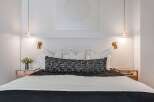 Experience modern luxury in this beautifully appointed bedroom, featuring a king-sized bed with a textured headboard and elegant brass sconces.