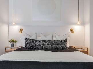 Experience modern luxury in this beautifully appointed bedroom, featuring a king-sized bed with a textured headboard and elegant brass sconces.
