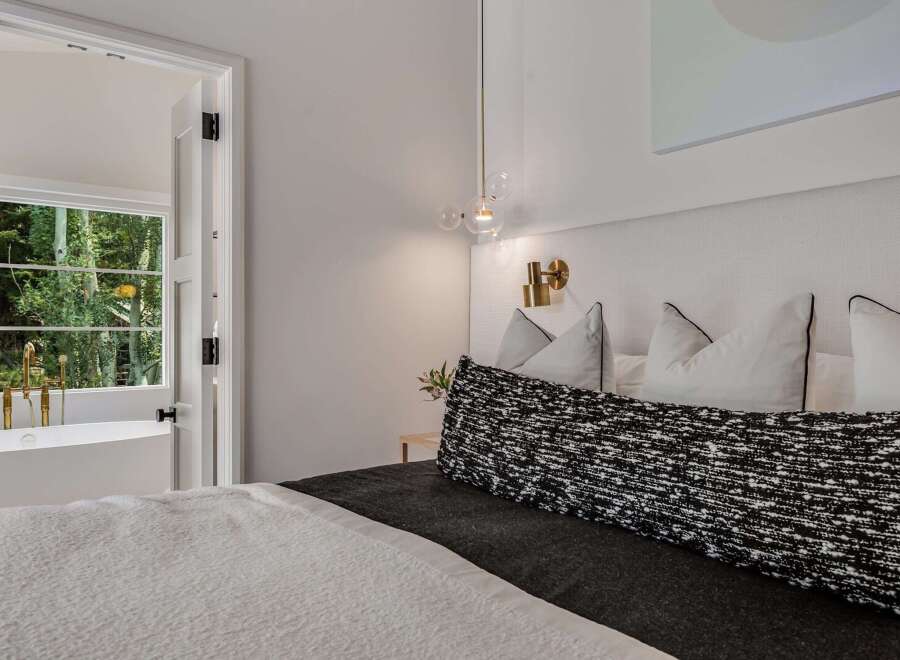 Experience luxury living with this stunning bedroom featuring a plush king-sized bed and a unique adjoining bathroom with a freestanding tub and a view of lush greenery.