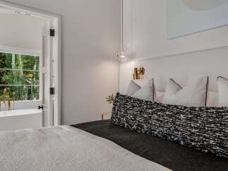 Experience luxury living with this stunning bedroom featuring a plush king-sized bed and a unique adjoining bathroom with a freestanding tub and a view of lush greenery.
