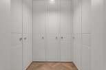 Step into this elegant walk-in closet featuring custom built-in cabinetry with textured white panels and sleek brass hardware.