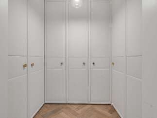Step into this elegant walk-in closet featuring custom built-in cabinetry with textured white panels and sleek brass hardware.