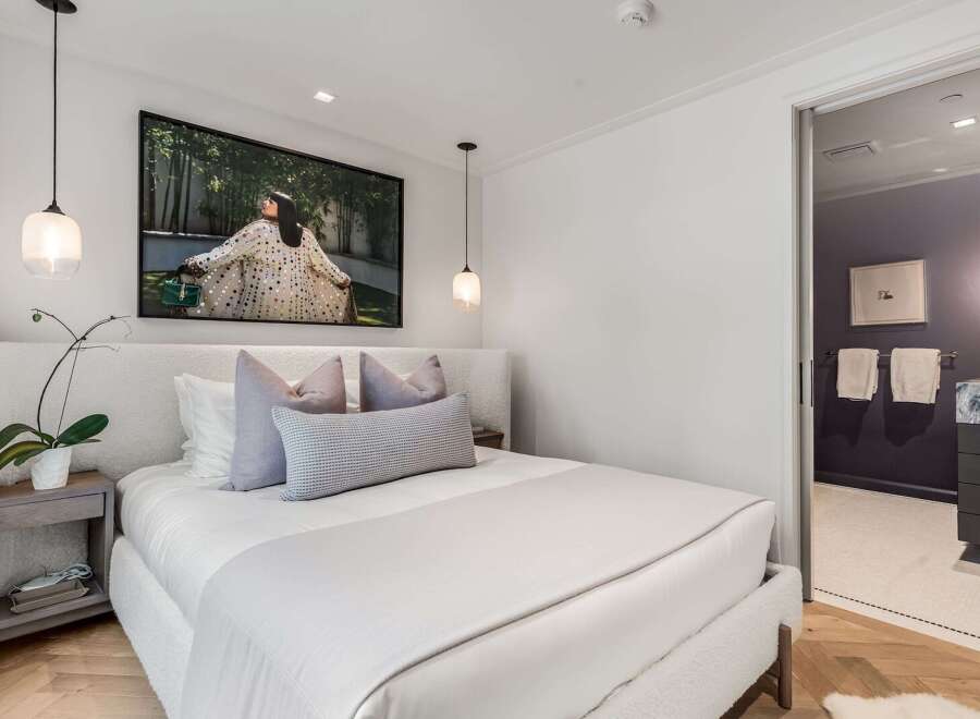 Experience modern luxury in this serene bedroom, featuring a plush, textured headboard and a striking piece of art above the bed.