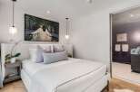 Experience modern luxury in this serene bedroom, featuring a plush, textured headboard and a striking piece of art above the bed.