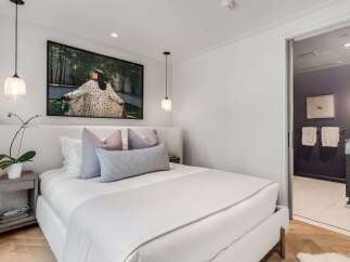 Experience modern luxury in this serene bedroom, featuring a plush, textured headboard and a striking piece of art above the bed.