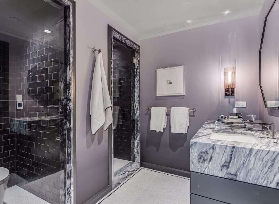 Experience modern luxury in this stunning bathroom, featuring a sleek glass-enclosed shower with dark subway tiles and a sophisticated marble vanity.